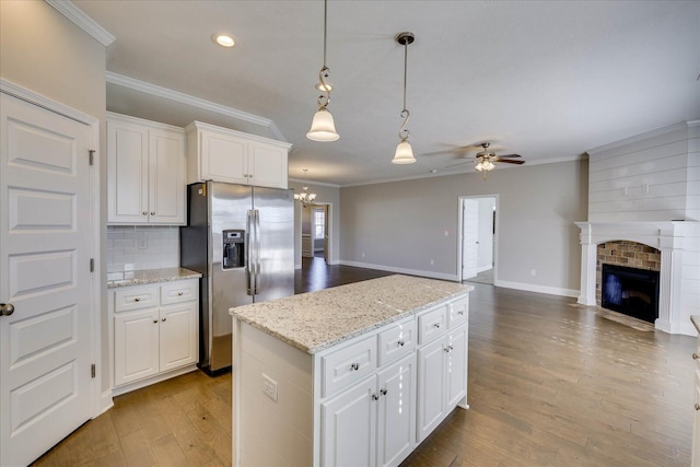 kitchen featuring a brick fireplace, decorative backsplash, stainless steel fridge with ice dispenser, white cabinets, and ceiling fan with notable chandelier