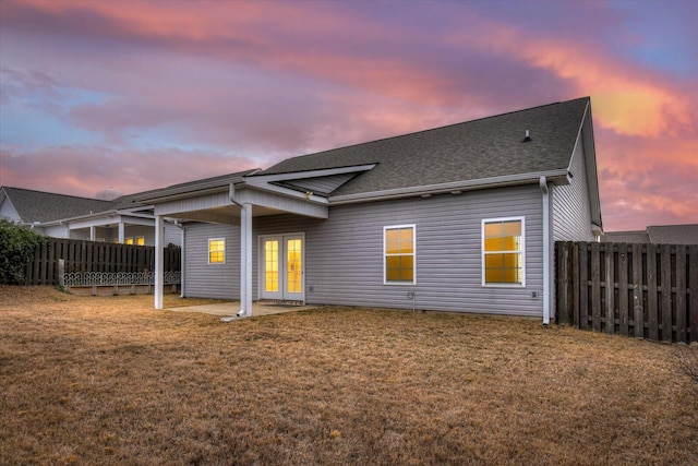 back house at dusk featuring a lawn