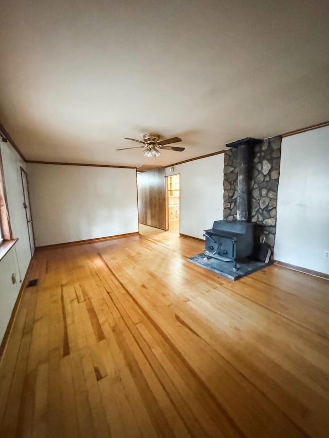 unfurnished living room featuring wood-type flooring, a wood stove, ceiling fan, and crown molding