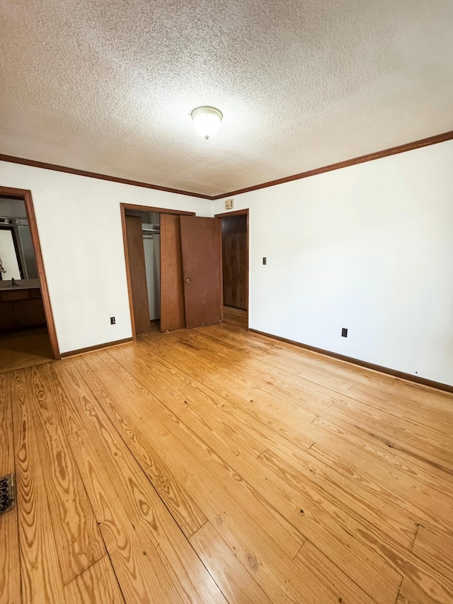 unfurnished bedroom with light wood-type flooring, ensuite bath, ornamental molding, a textured ceiling, and a closet