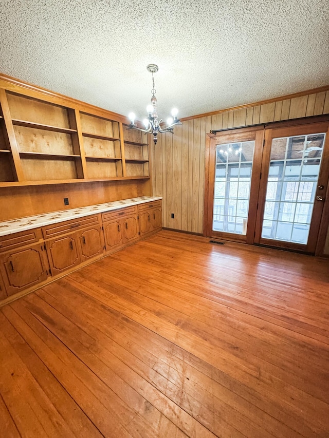 unfurnished dining area featuring a textured ceiling, light hardwood / wood-style floors, an inviting chandelier, and wooden walls