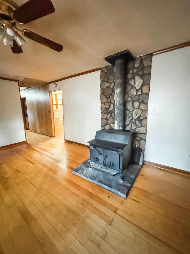 unfurnished living room with wood-type flooring, a wood stove, ceiling fan, and ornamental molding