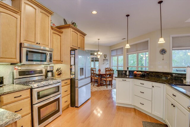 kitchen with dark stone countertops, light brown cabinets, pendant lighting, and appliances with stainless steel finishes