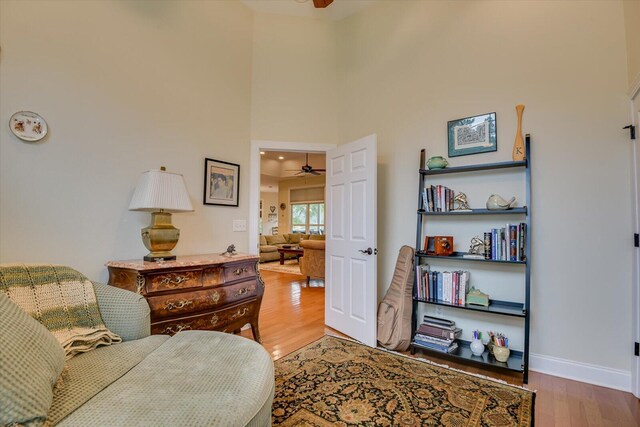 living area with wood-type flooring, a towering ceiling, and ceiling fan