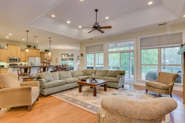 living room featuring a raised ceiling, ceiling fan, a healthy amount of sunlight, and light hardwood / wood-style floors