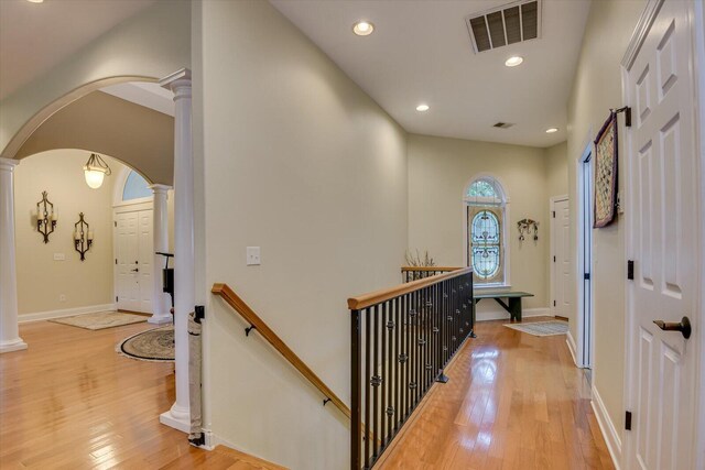 hallway featuring light wood-type flooring and decorative columns