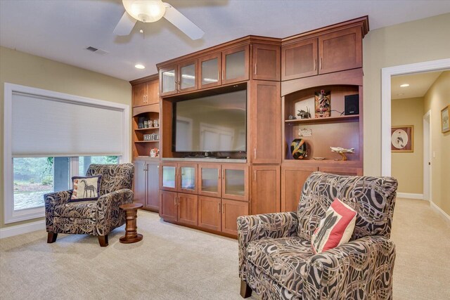 living area with built in shelves, light colored carpet, and ceiling fan