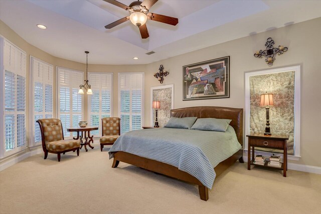 bedroom with carpet flooring, ceiling fan with notable chandelier, and a tray ceiling