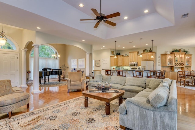 living room featuring decorative columns, light hardwood / wood-style flooring, a high ceiling, and ceiling fan with notable chandelier