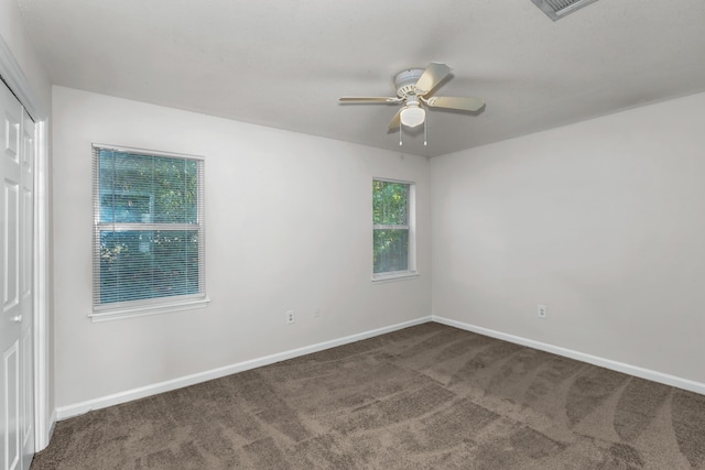 spare room featuring dark carpet, plenty of natural light, and ceiling fan