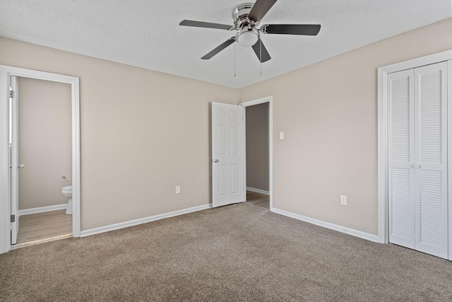 unfurnished bedroom featuring a textured ceiling, baseboards, a closet, carpet, and ensuite bath