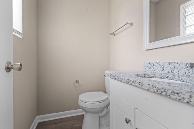 half bathroom featuring toilet, baseboards, wood finished floors, and vanity