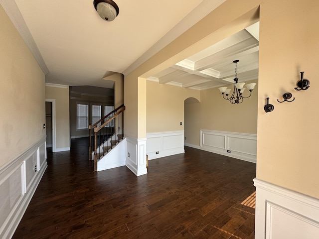 empty room with arched walkways, dark wood-style flooring, coffered ceiling, stairway, and beam ceiling