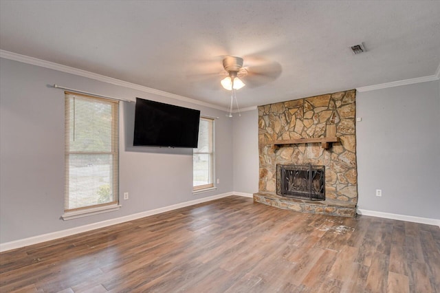 unfurnished living room with a stone fireplace, ceiling fan, plenty of natural light, and crown molding