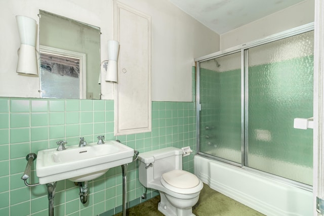 bathroom featuring toilet, bath / shower combo with glass door, and tile walls