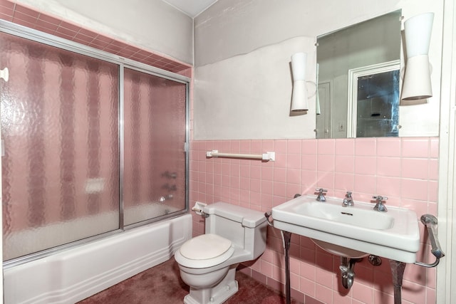 full bathroom featuring sink, toilet, tile walls, and bath / shower combo with glass door