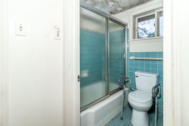 bathroom featuring toilet, tile walls, and bath / shower combo with glass door