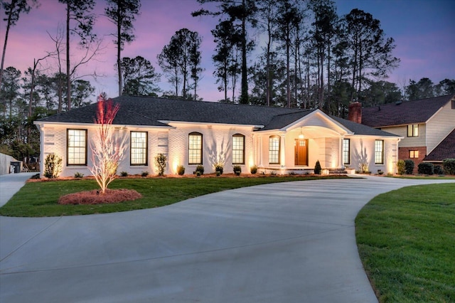 view of front of property featuring driveway, brick siding, a chimney, and a lawn