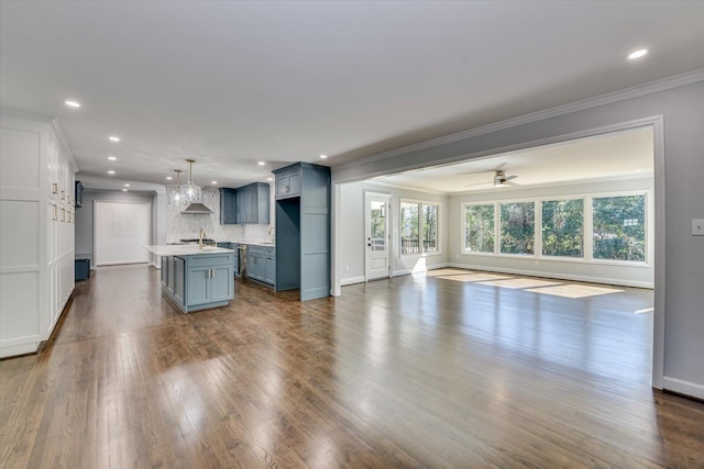 kitchen with a kitchen island with sink, dark wood-style flooring, open floor plan, backsplash, and crown molding