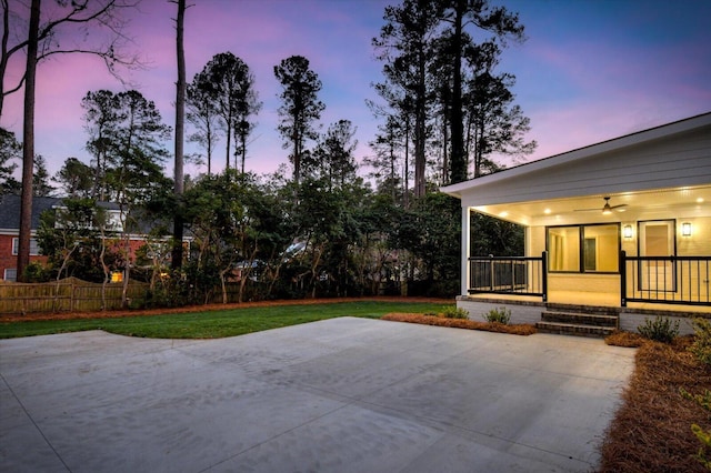 patio terrace at dusk featuring covered porch, ceiling fan, a yard, and fence