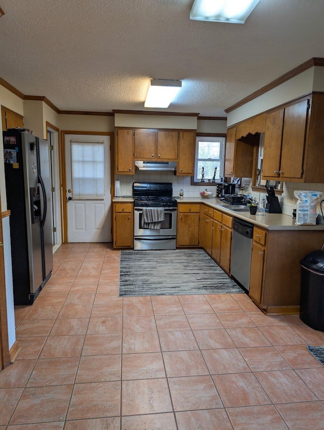 kitchen with backsplash, under cabinet range hood, ornamental molding, appliances with stainless steel finishes, and brown cabinetry