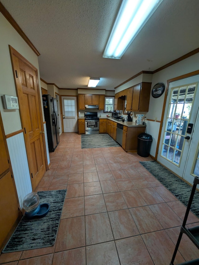 kitchen featuring a wainscoted wall, stainless steel appliances, light countertops, a textured ceiling, and crown molding