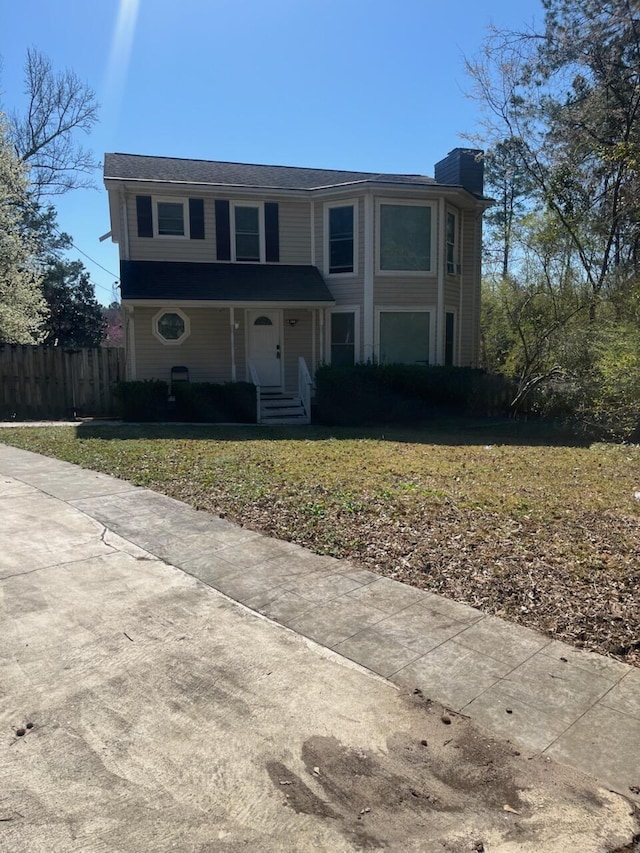 view of front of house with a front yard, a chimney, and fence