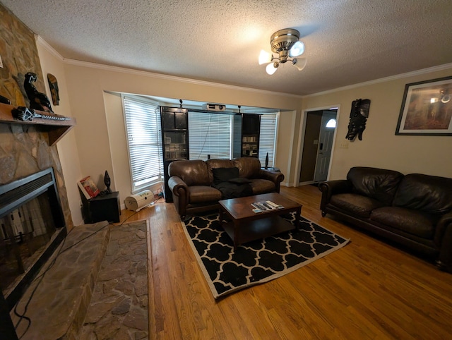 living room featuring a stone fireplace, crown molding, wood finished floors, and a textured ceiling