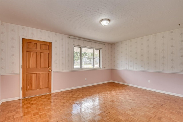 unfurnished room featuring wallpapered walls, a wainscoted wall, and a textured ceiling