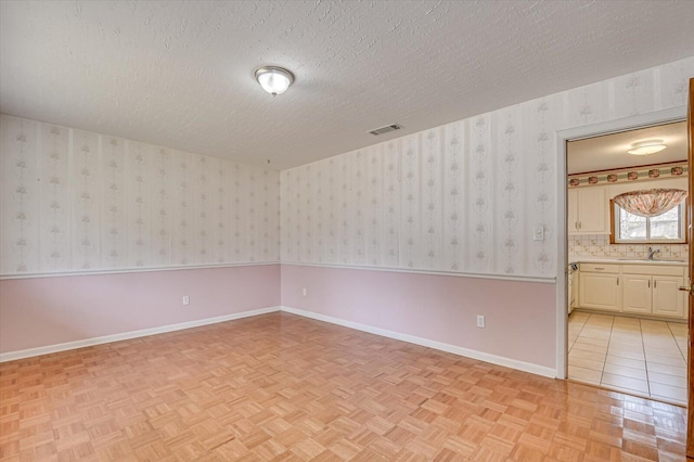 unfurnished room with wallpapered walls, baseboards, visible vents, and a textured ceiling