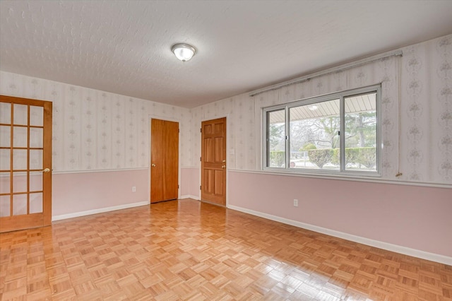 empty room with a textured ceiling, wallpapered walls, and baseboards