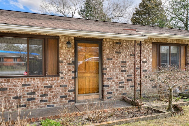 view of exterior entry featuring brick siding, crawl space, and a shingled roof