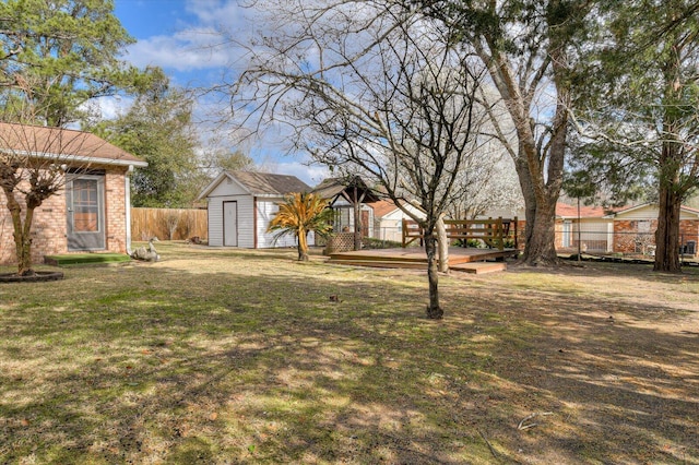 view of yard with an outbuilding, a wooden deck, a storage unit, and fence