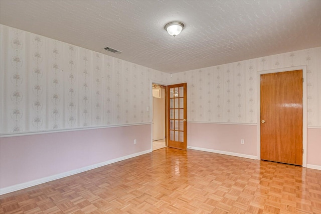 spare room featuring a wainscoted wall, baseboards, visible vents, wallpapered walls, and a textured ceiling