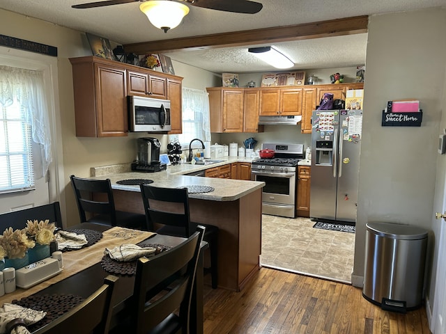 kitchen with under cabinet range hood, appliances with stainless steel finishes, a sink, a ceiling fan, and a peninsula
