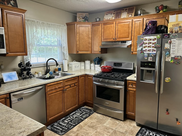 kitchen with a sink, appliances with stainless steel finishes, light countertops, under cabinet range hood, and brown cabinetry