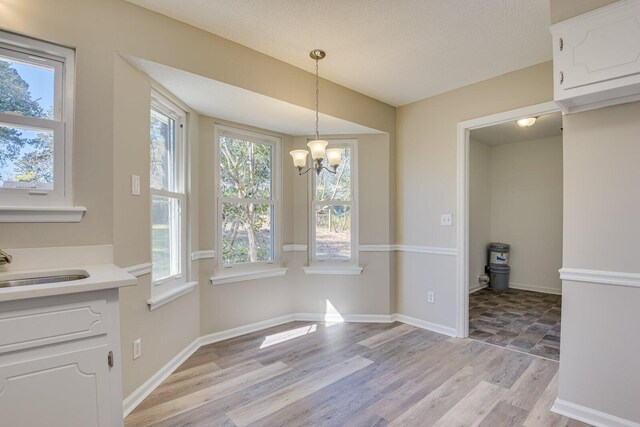 unfurnished dining area with a healthy amount of sunlight, a notable chandelier, light wood-style floors, and a sink