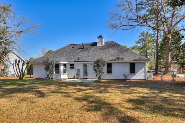 rear view of house with fence, roof with shingles, a lawn, a chimney, and a patio area