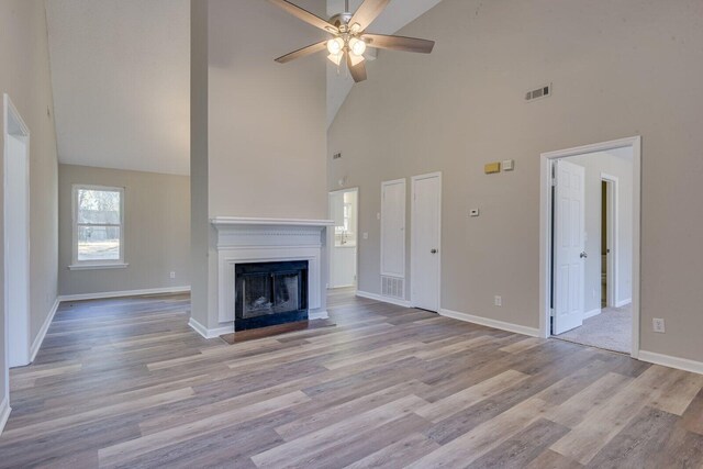 unfurnished living room featuring wood finished floors, visible vents, baseboards, a fireplace with raised hearth, and ceiling fan