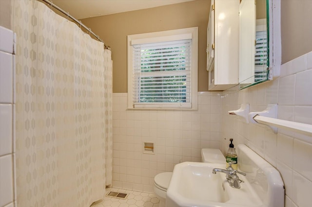 full bathroom featuring tile patterned flooring, toilet, a sink, visible vents, and tile walls