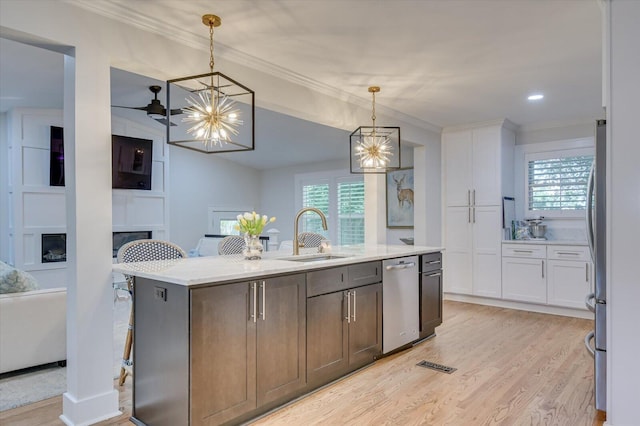 kitchen with a large fireplace, light wood-style flooring, a kitchen island with sink, stainless steel appliances, and a sink