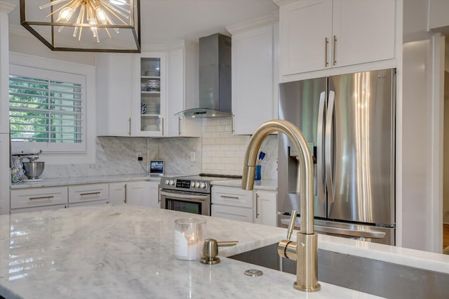 kitchen featuring white cabinets, wall chimney range hood, stainless steel appliances, and decorative backsplash