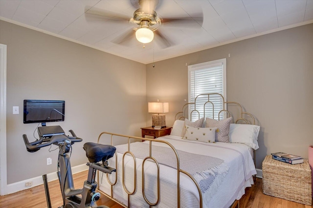 bedroom with a ceiling fan, baseboards, wood finished floors, and ornamental molding