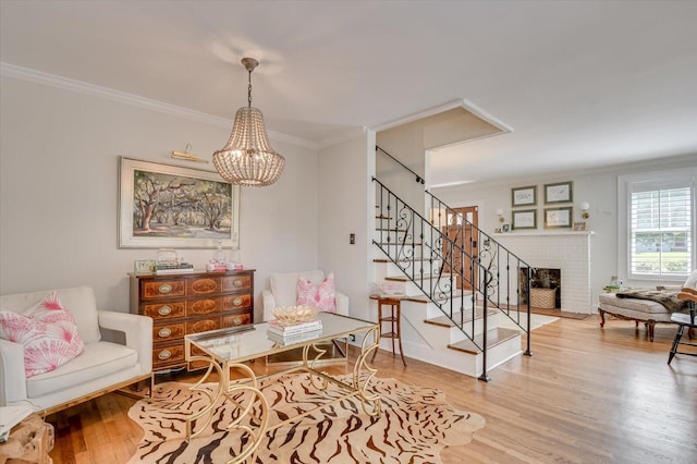 sitting room with wood finished floors, ornamental molding, stairway, a brick fireplace, and an inviting chandelier