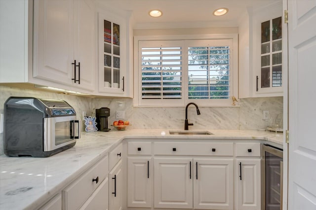 kitchen featuring beverage cooler, backsplash, a sink, and white cabinetry