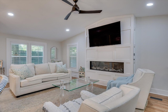 living room featuring recessed lighting, wood finished floors, visible vents, vaulted ceiling, and a glass covered fireplace