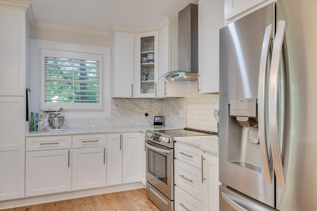 kitchen featuring wall chimney range hood, white cabinetry, appliances with stainless steel finishes, and ornamental molding