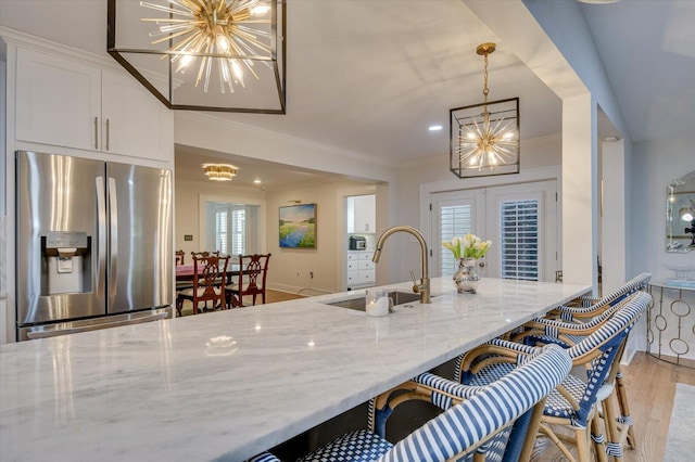 kitchen with light stone counters, french doors, a notable chandelier, stainless steel refrigerator with ice dispenser, and a sink