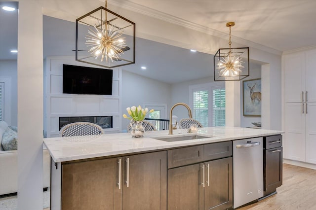 kitchen featuring crown molding, a glass covered fireplace, a sink, light stone countertops, and dishwasher