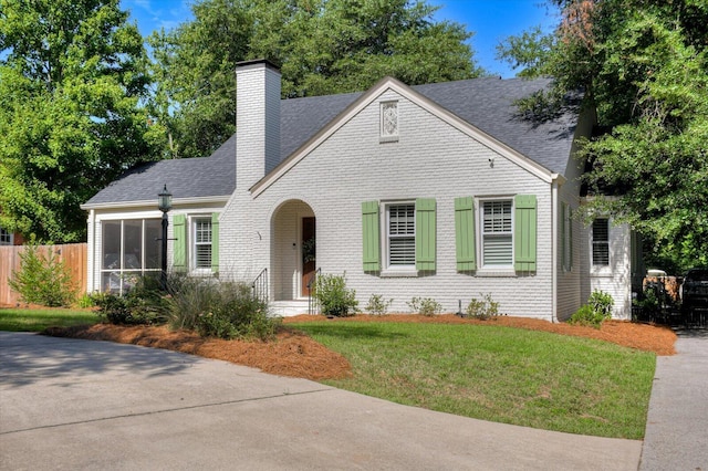 view of front of house featuring brick siding, a chimney, roof with shingles, fence, and a front yard